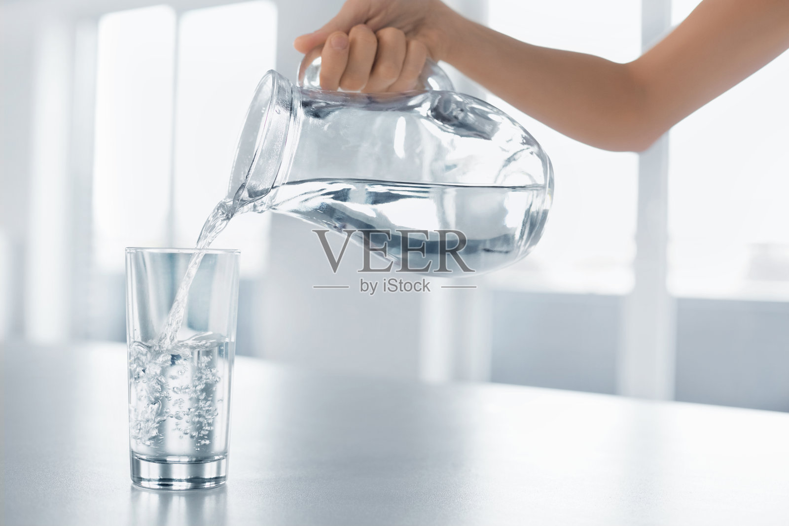 喝水。女人的手把水从水罐倒进玻璃杯里照片摄影图片
