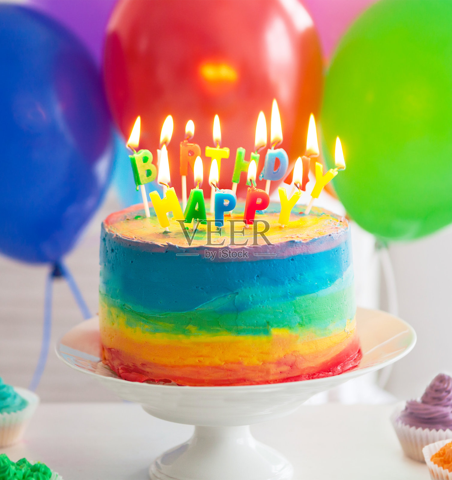 装饰着生日蜡烛的彩虹蛋糕和纸杯蛋糕照片摄影图片
