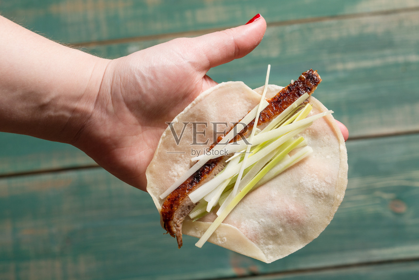 女人手里拿着煎饼，里面有北京烤鸭肉、洋葱和黄瓜片。俯视图照片摄影图片