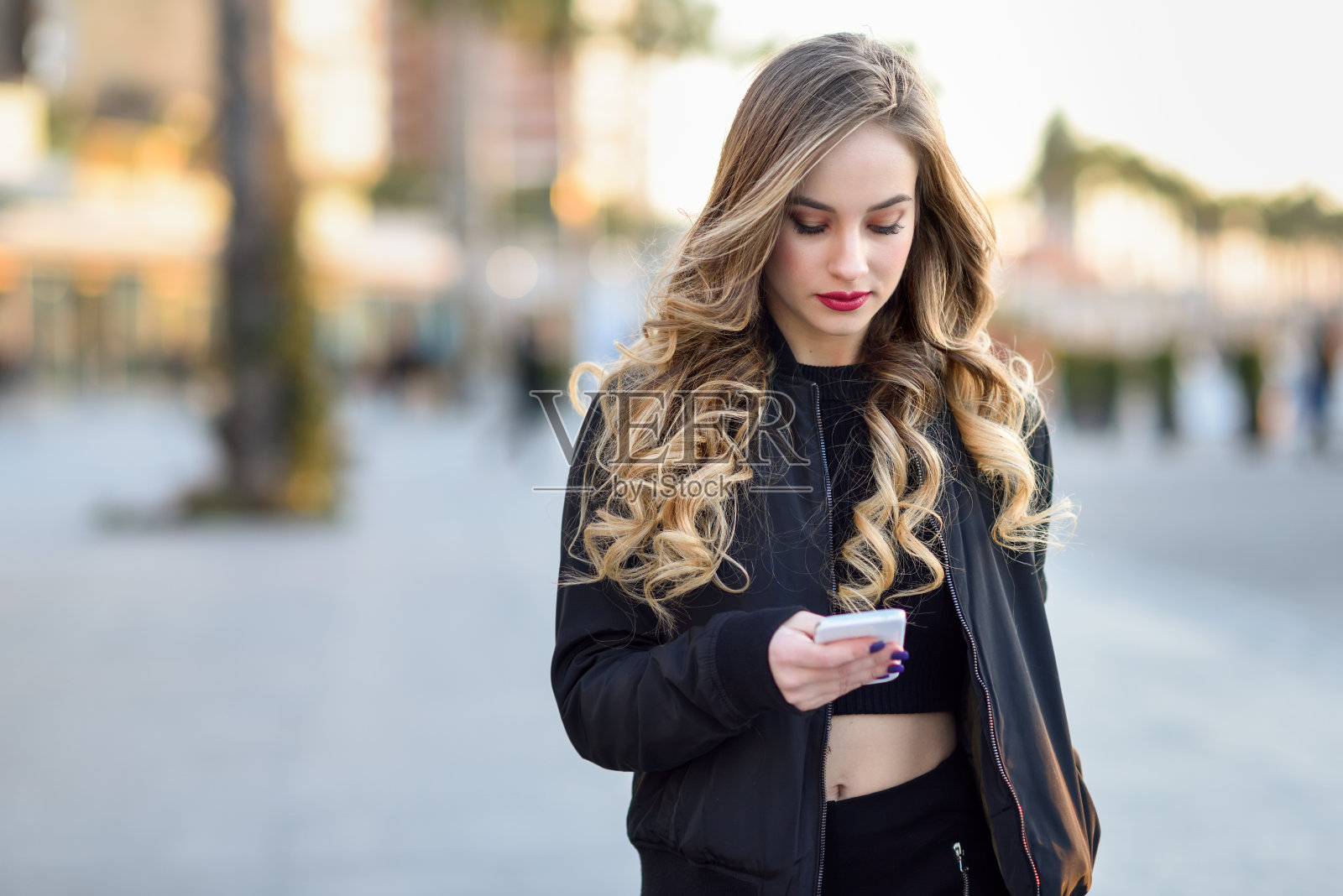 一个金发女人用她的智能手机在城市背景下发短信照片摄影图片