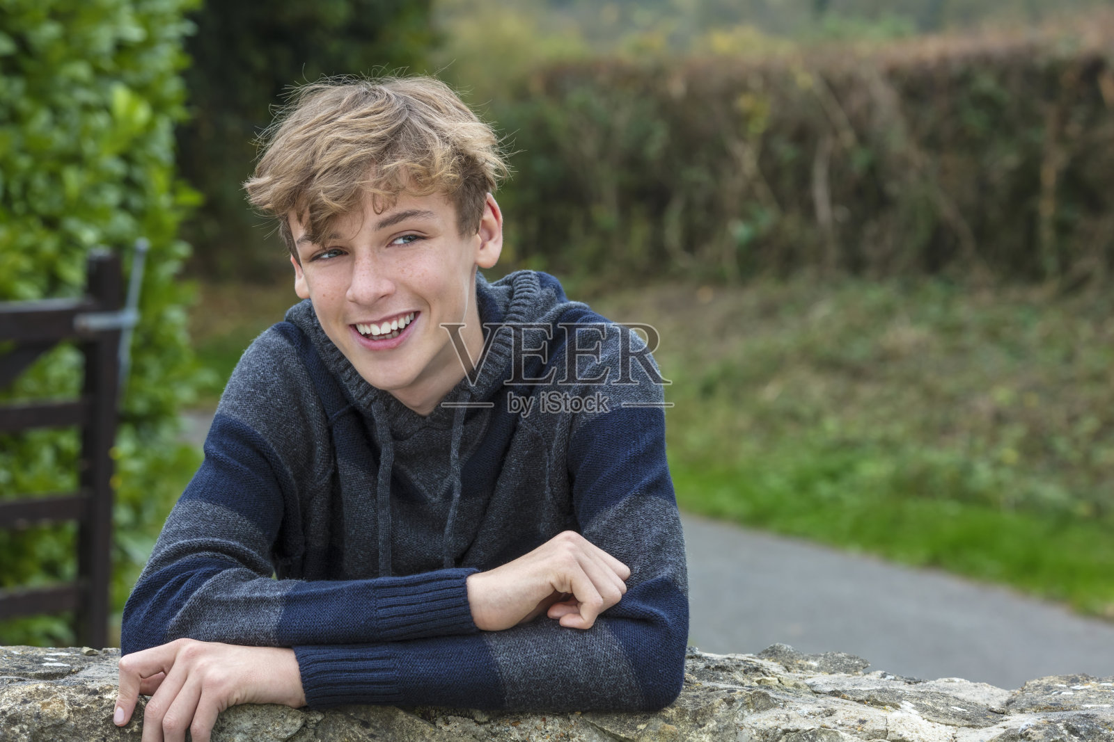 年轻快乐的笑着微笑的少年男孩金发碧眼的孩子外倚着一堵墙在秋天秋天的阳光照片摄影图片