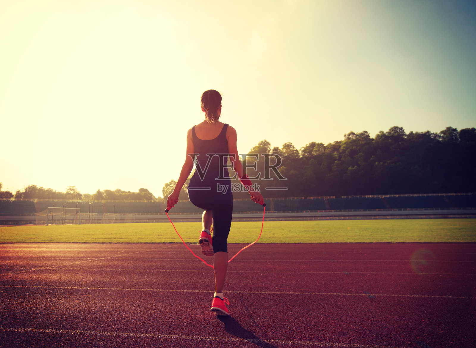 一个年轻女子在阳光明媚的早晨在体育场的跑道上跳绳照片摄影图片
