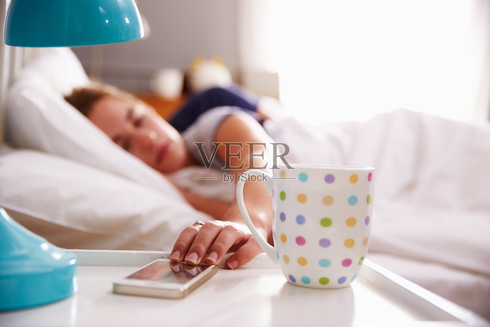 一个女人躺在床上拿床头柜上的手机照片摄影图片