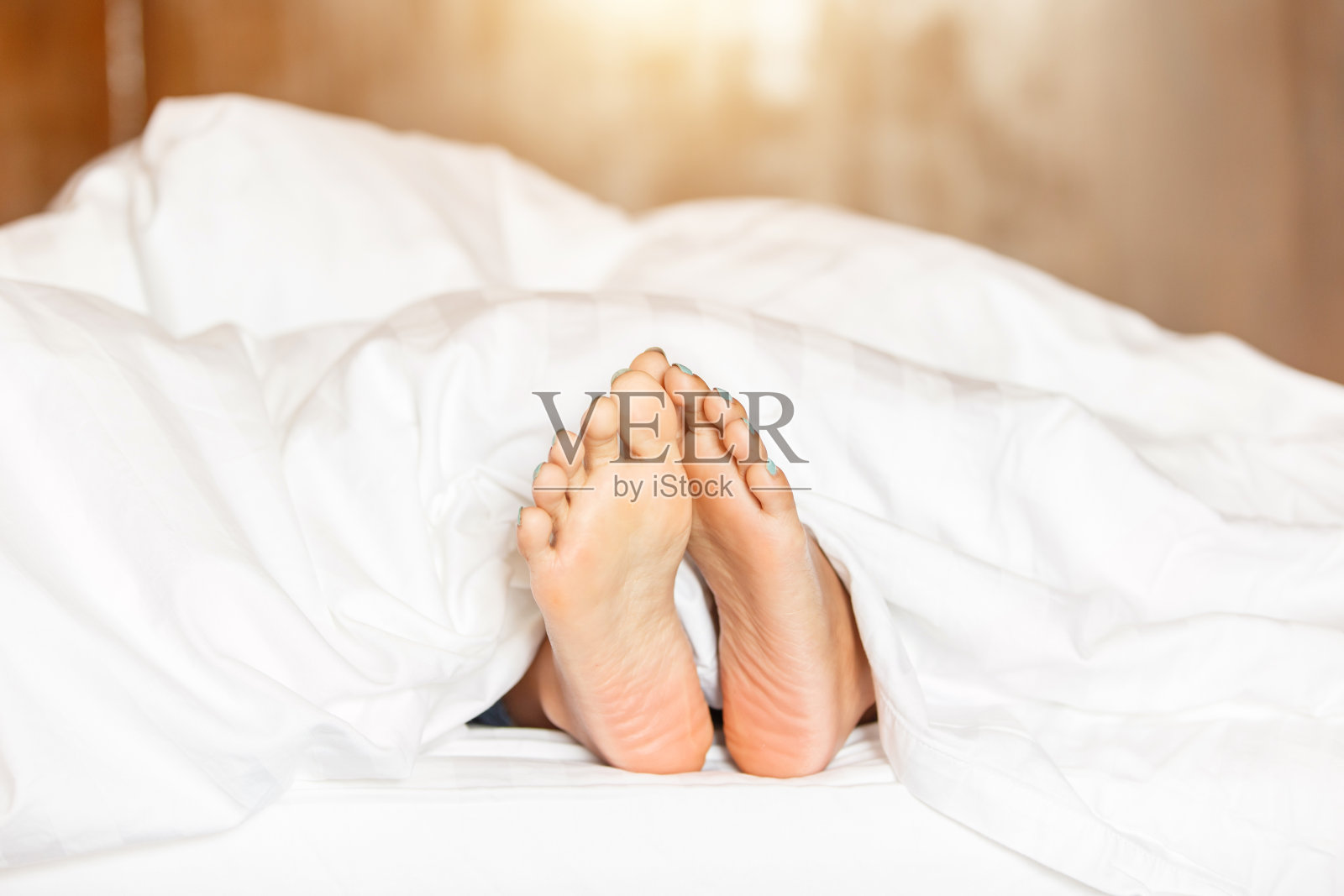 女人脚下白色毯子侧视。美丽的年轻女子脚与蓝色足疗在床上。睡在白色毯子下的女人的腿照片摄影图片