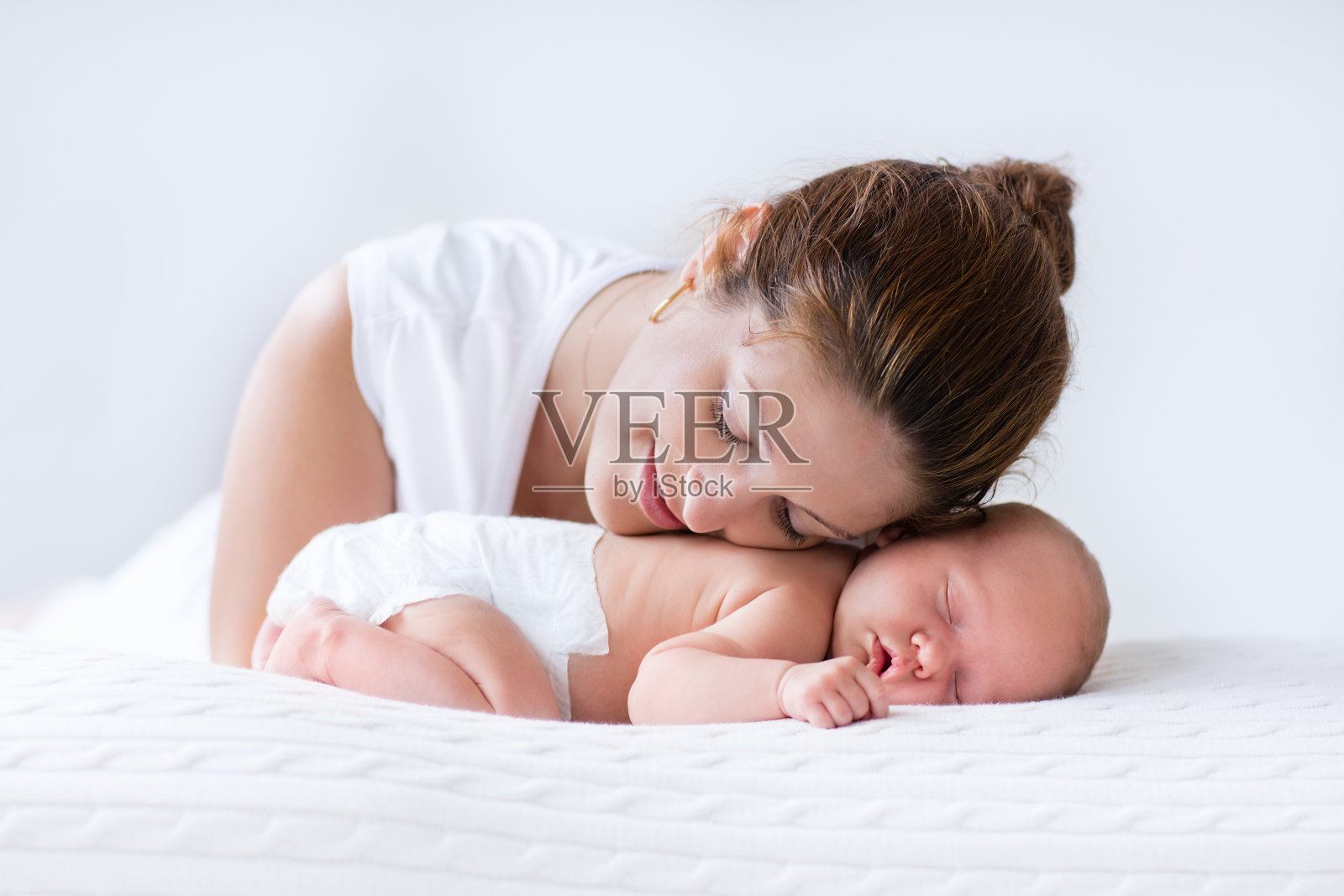 年轻的母亲和刚出生的婴儿在白色的卧室照片摄影图片