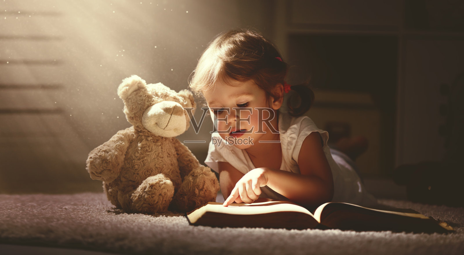 一个小女孩在黑暗的家里读一本魔法书照片摄影图片