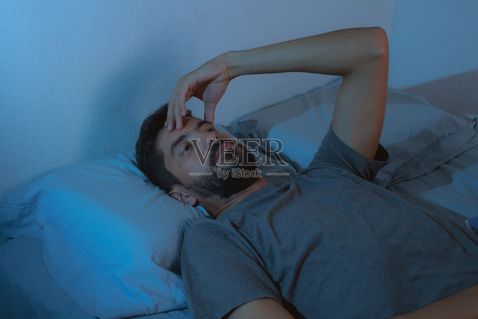 年轻的胡子男人醒着躺在床上照片摄影图片