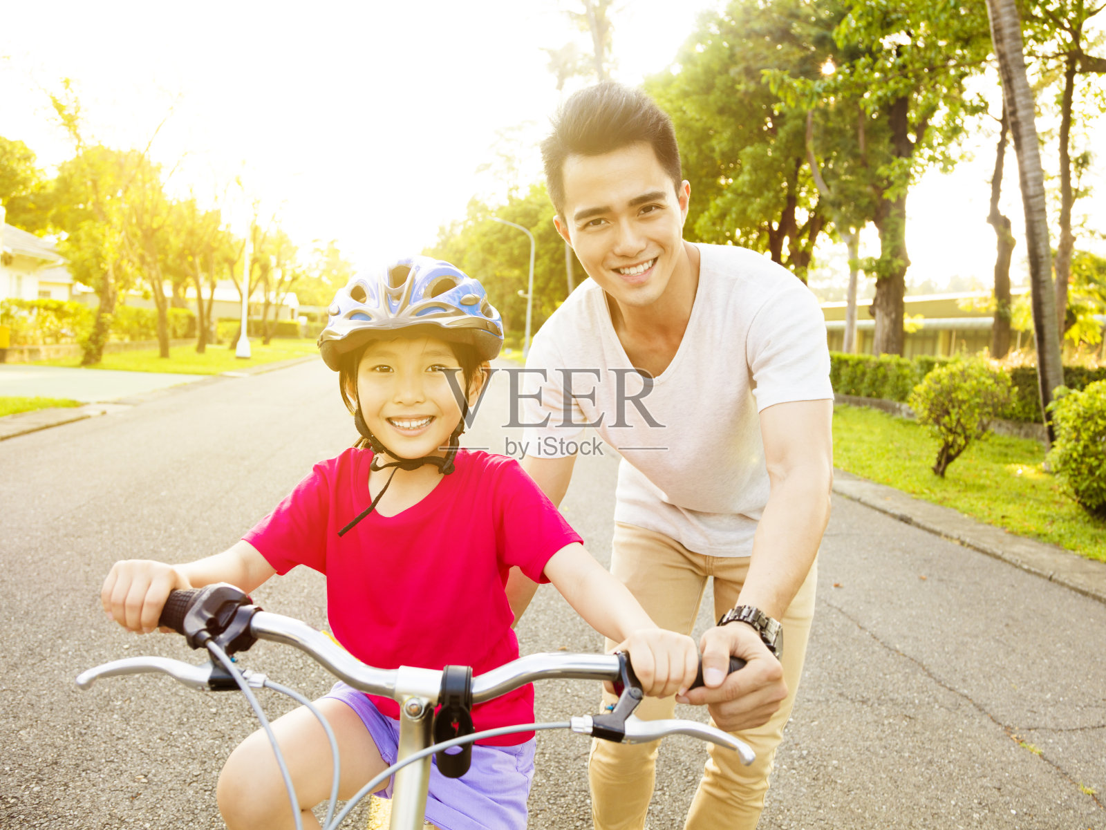 快乐的小女孩跟着爸爸练习骑自行车照片摄影图片