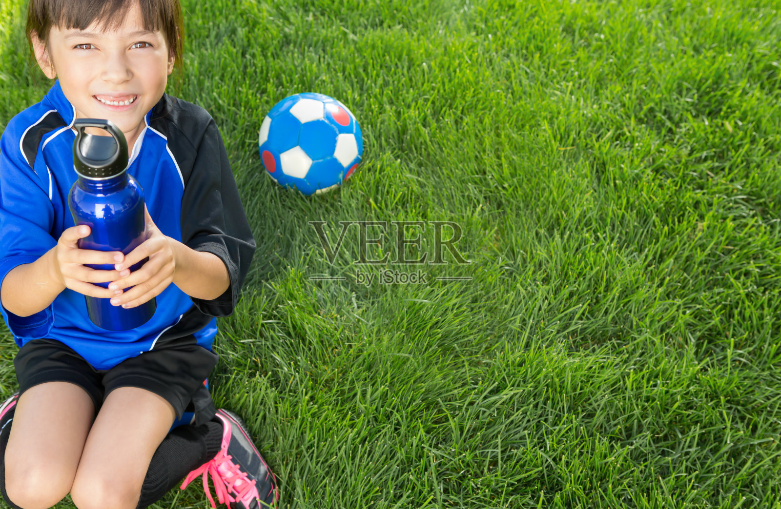 一个小女孩坐在她的足球上喝着酒照片摄影图片