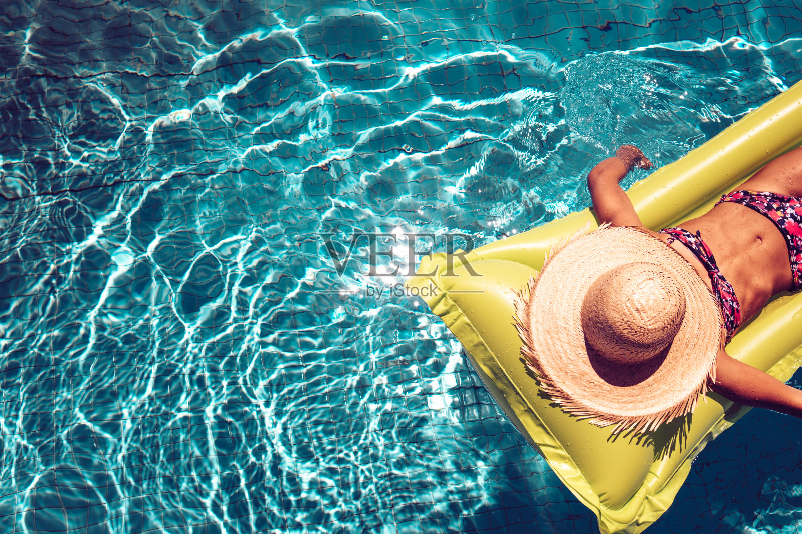 戴草帽的女孩在充气床上在蓝色的游泳池里游泳照片摄影图片