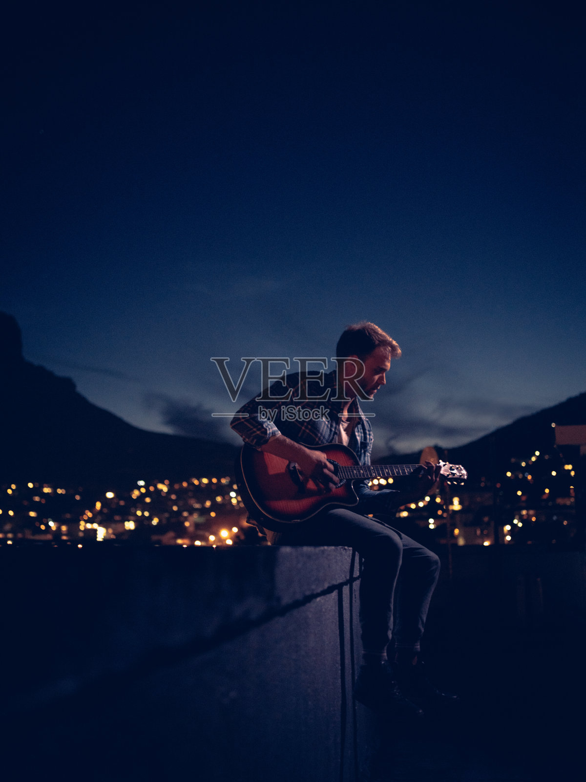 夏天的晚上，潮少年在屋顶上弹吉他照片摄影图片