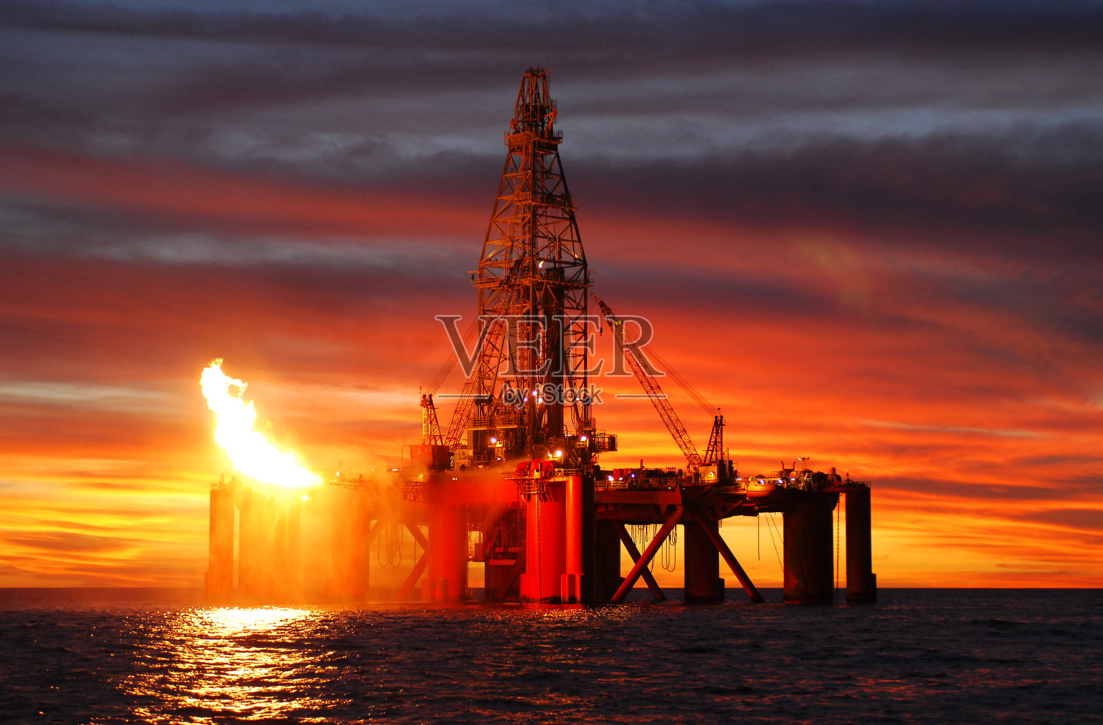 日落时海洋石油钻井平台的剪影。照片摄影图片