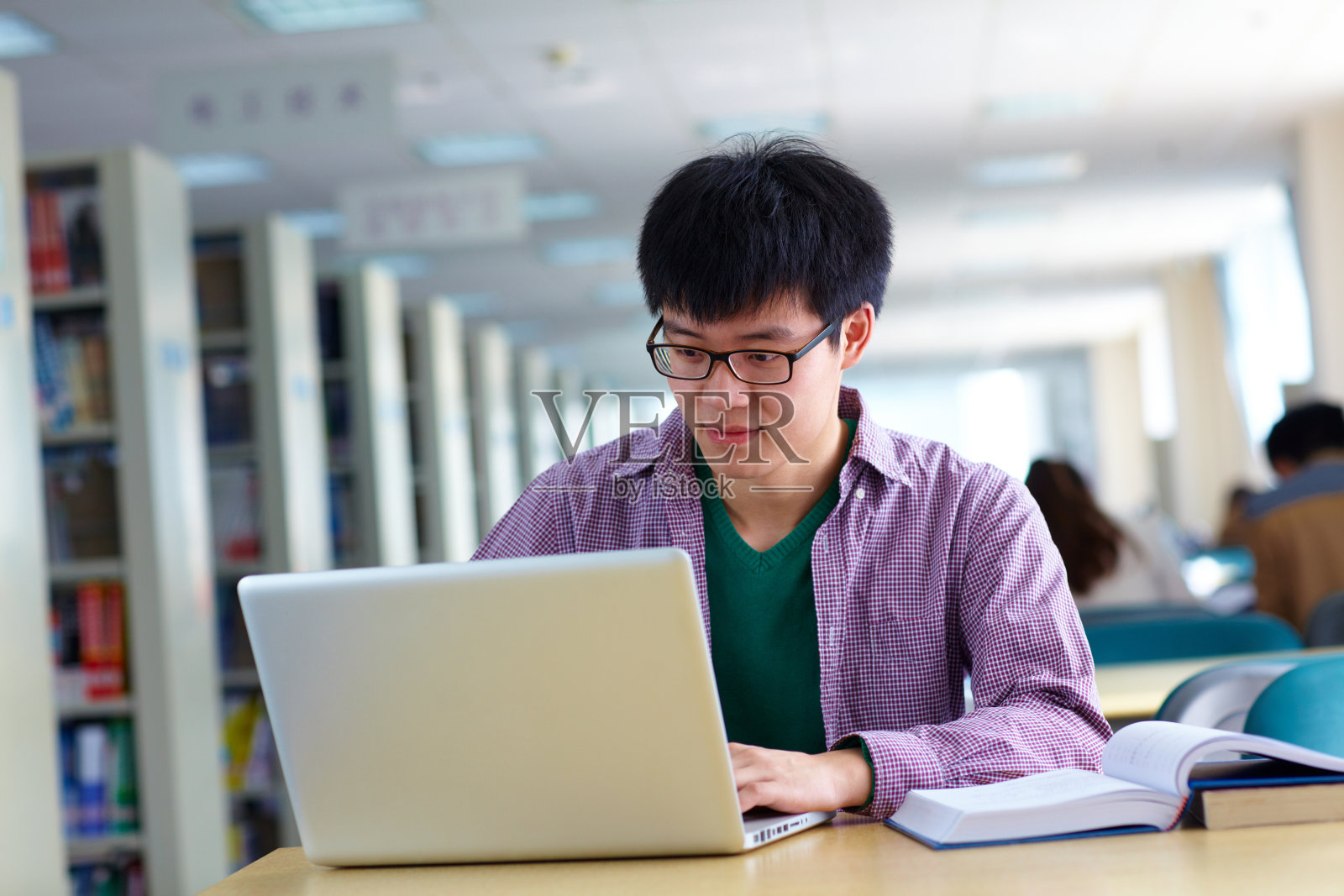一名亚洲男大学生在图书馆学习，桌上放着笔记本电脑照片摄影图片