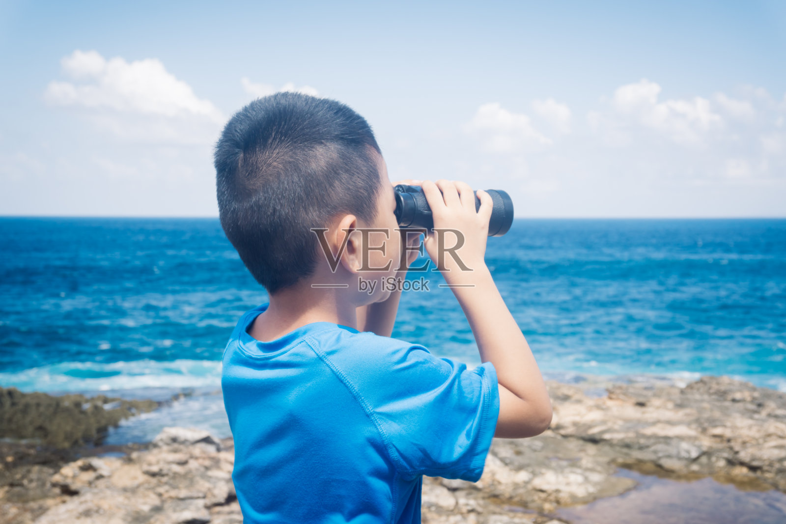 小男孩在悬崖上用双筒望远镜看照片摄影图片
