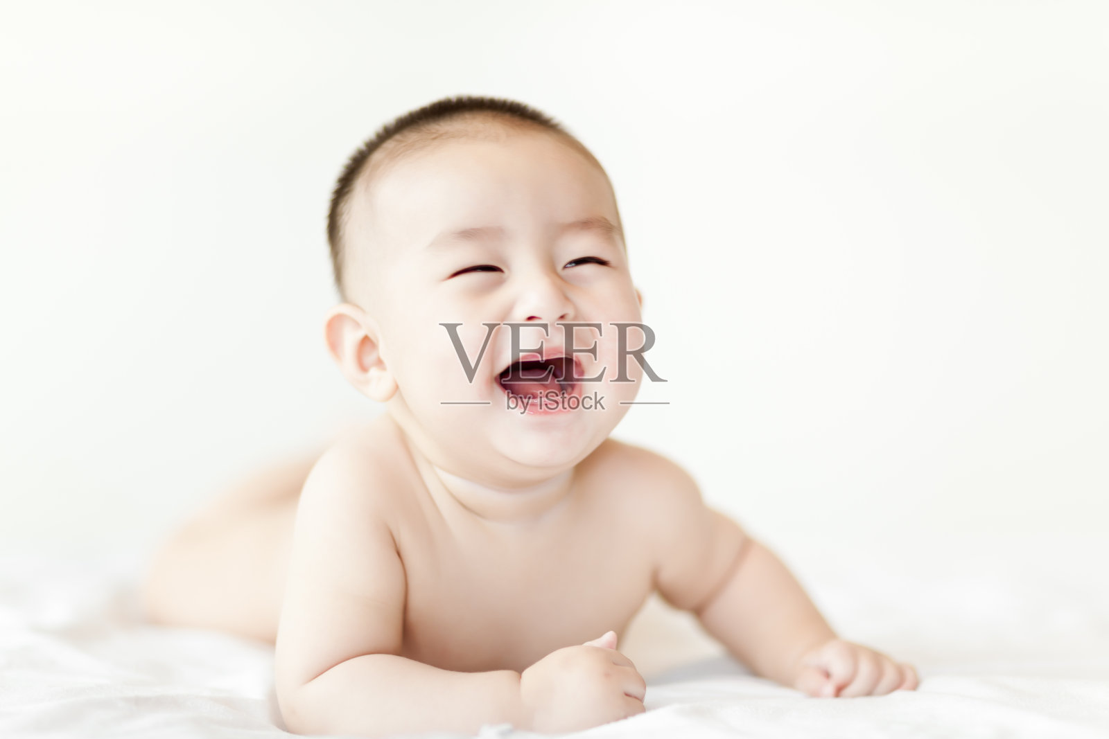 赤裸快乐的小男婴爬在白色的床上照片摄影图片