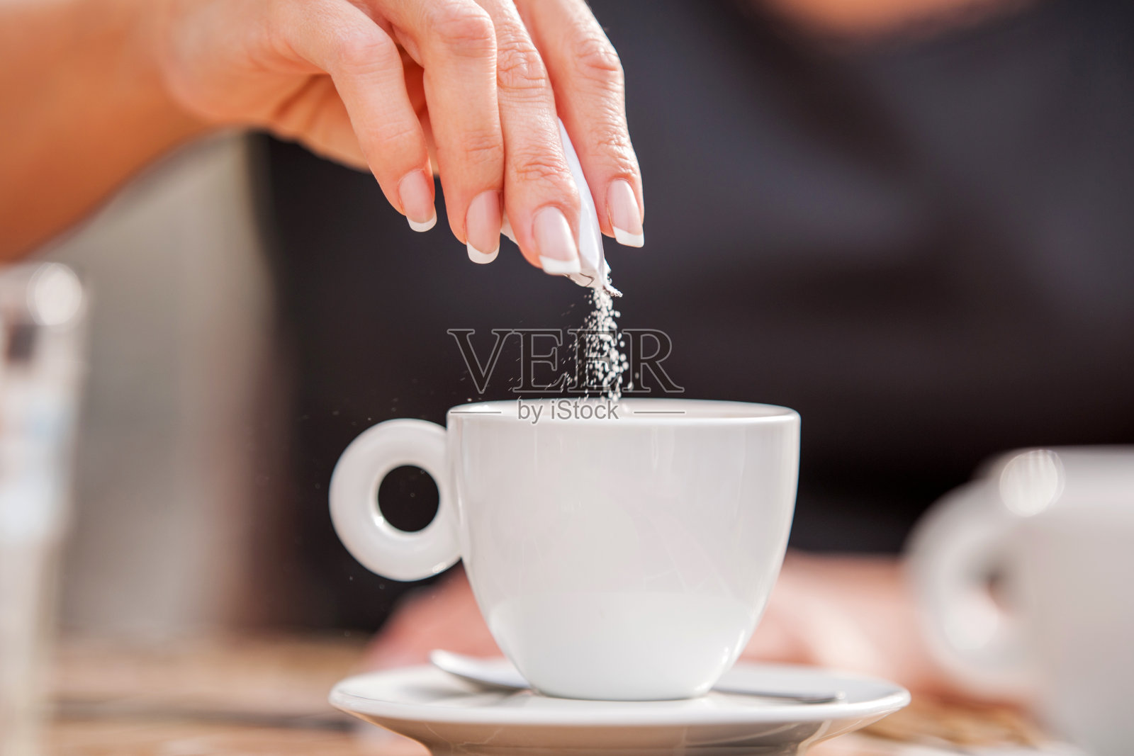 一个女人在咖啡杯里倒糖的特写。照片摄影图片