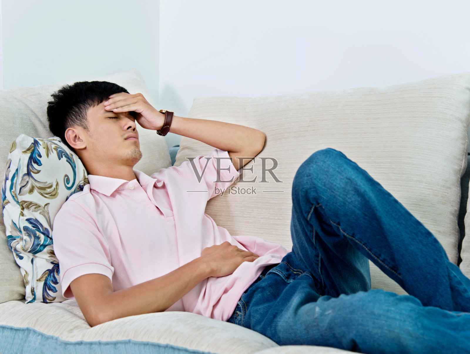 一个年轻的亚洲男人躺在沙发上，痛苦不堪照片摄影图片