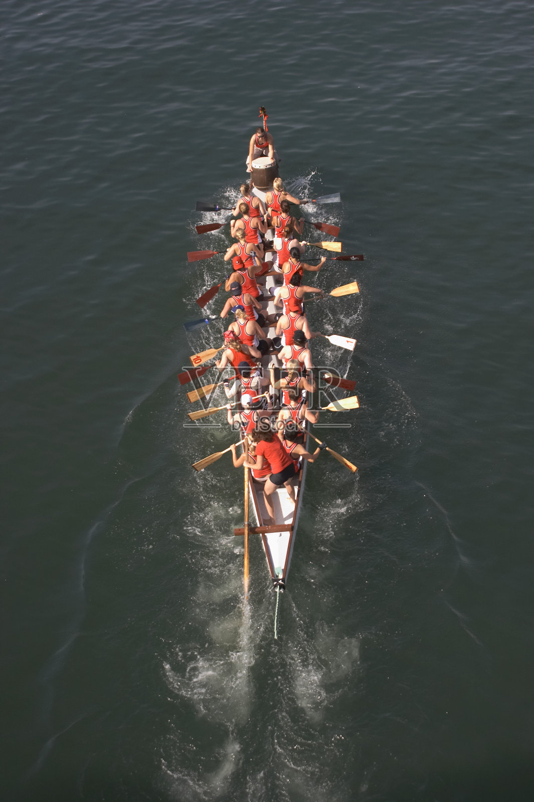 一艘由二十名穿着红上衣的人划着的大船照片摄影图片