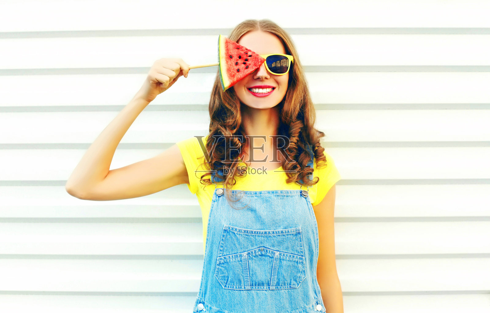 一名年轻的时尚女子面带微笑，在白色的背景上拿着一片冰淇淋形状的西瓜照片摄影图片