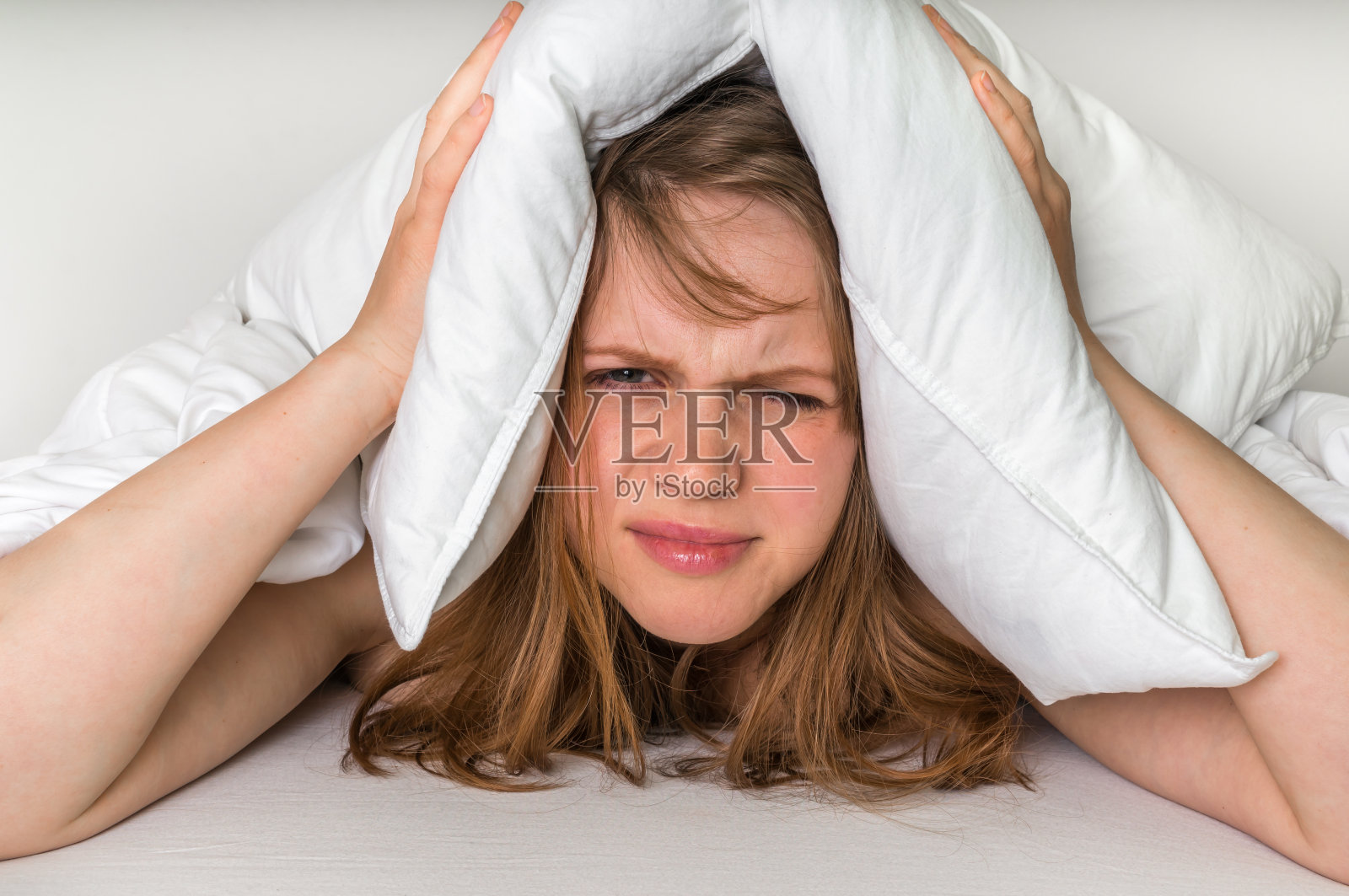因为噪音，躺在床上的女人用枕头捂住耳朵照片摄影图片
