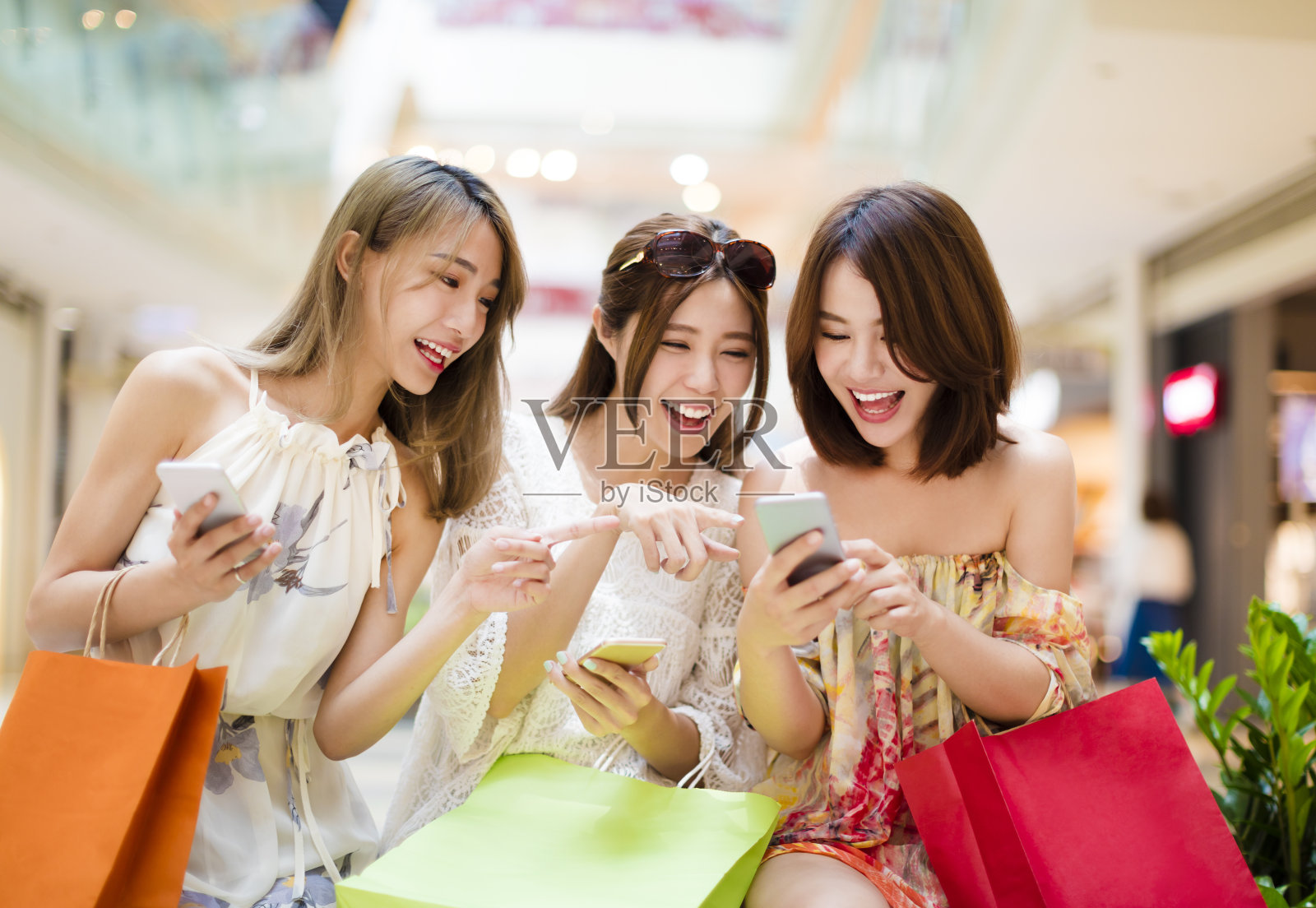 快乐的年轻女子在购物中心看智能手机照片摄影图片