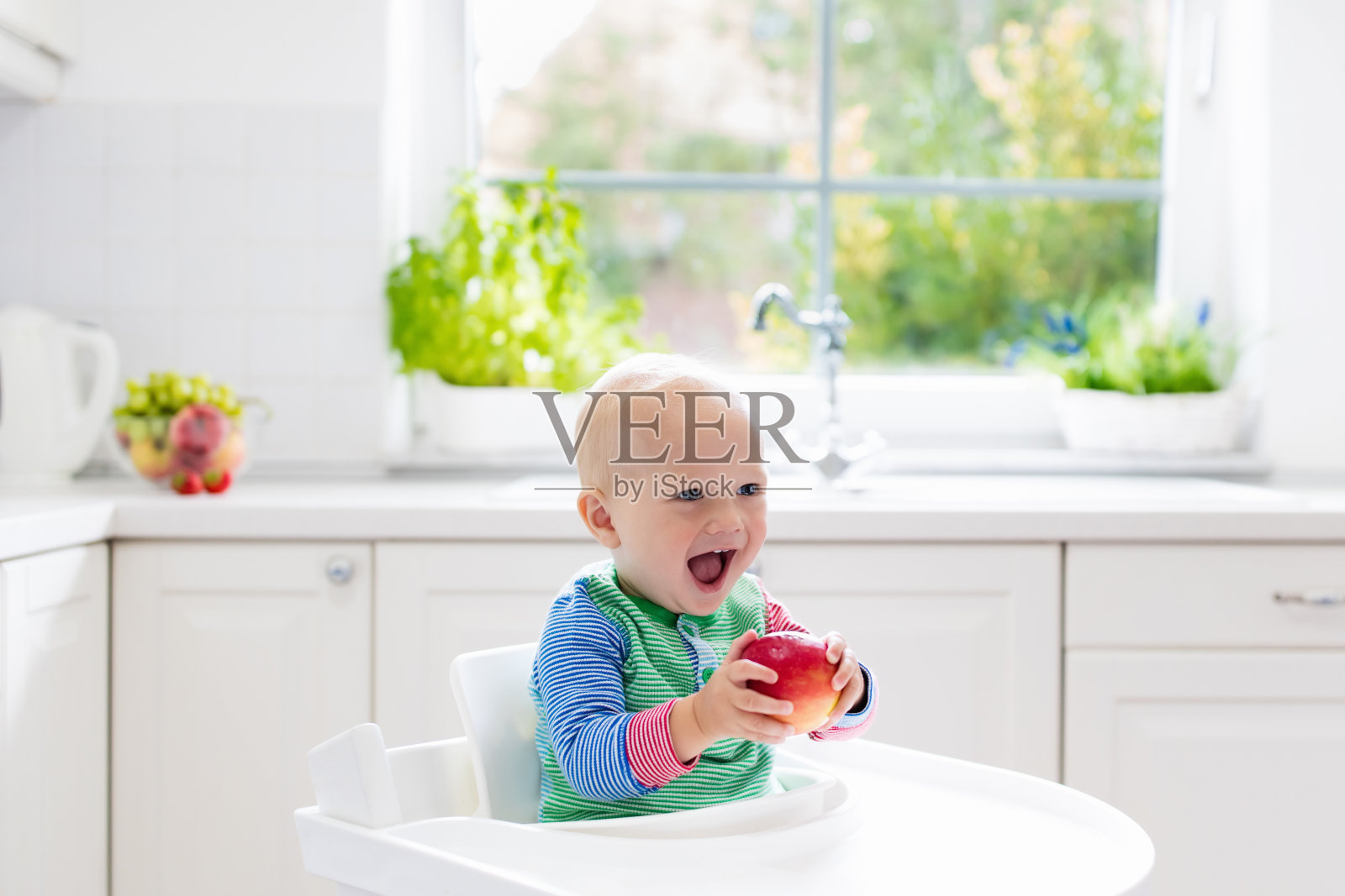 小男孩在家里白色的厨房里吃苹果照片摄影图片