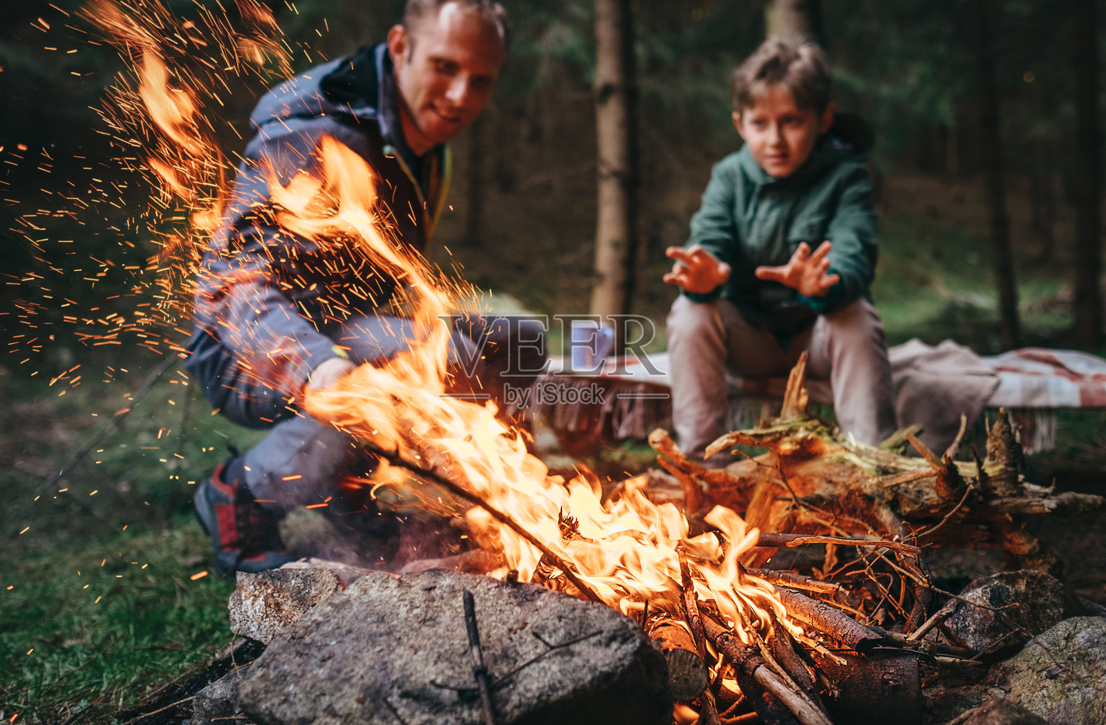 父亲和儿子在森林里的篝火旁取暖照片摄影图片