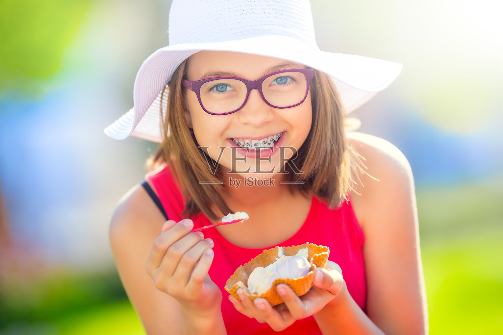 快乐的少女戴着牙套、眼镜和冰淇淋。一个微笑的漂亮的年轻女孩的肖像在夏天的服装与冰淇淋和牙齿矫正照片摄影图片