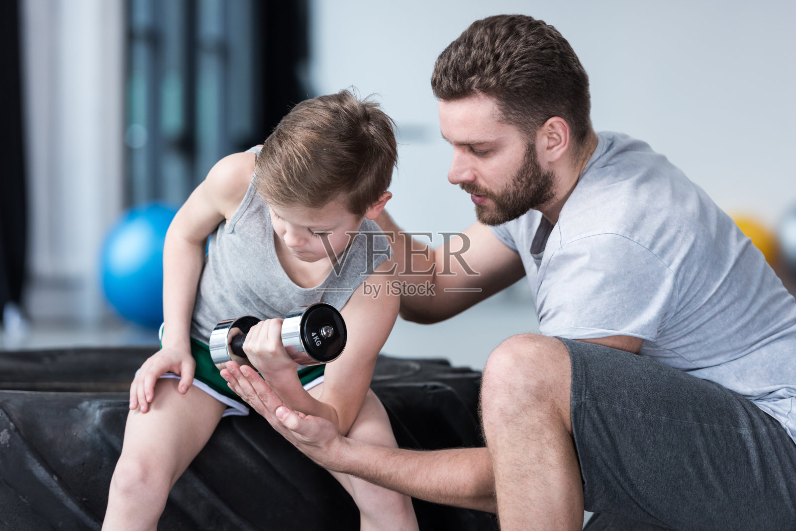 男孩在健身中心和教练一起用哑铃训练照片摄影图片