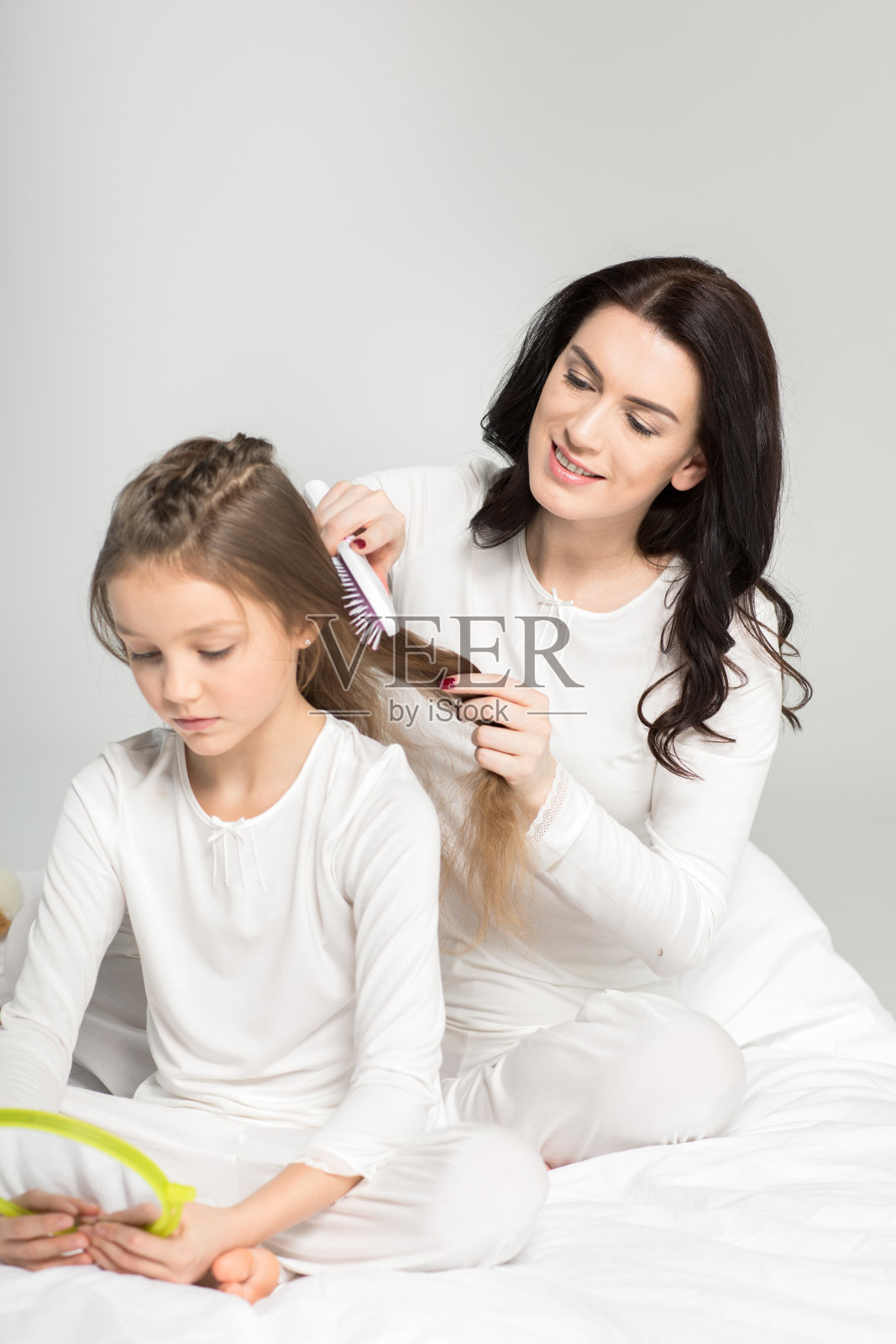 微笑的妈妈用手镜梳理可爱的小女儿的头发照片摄影图片