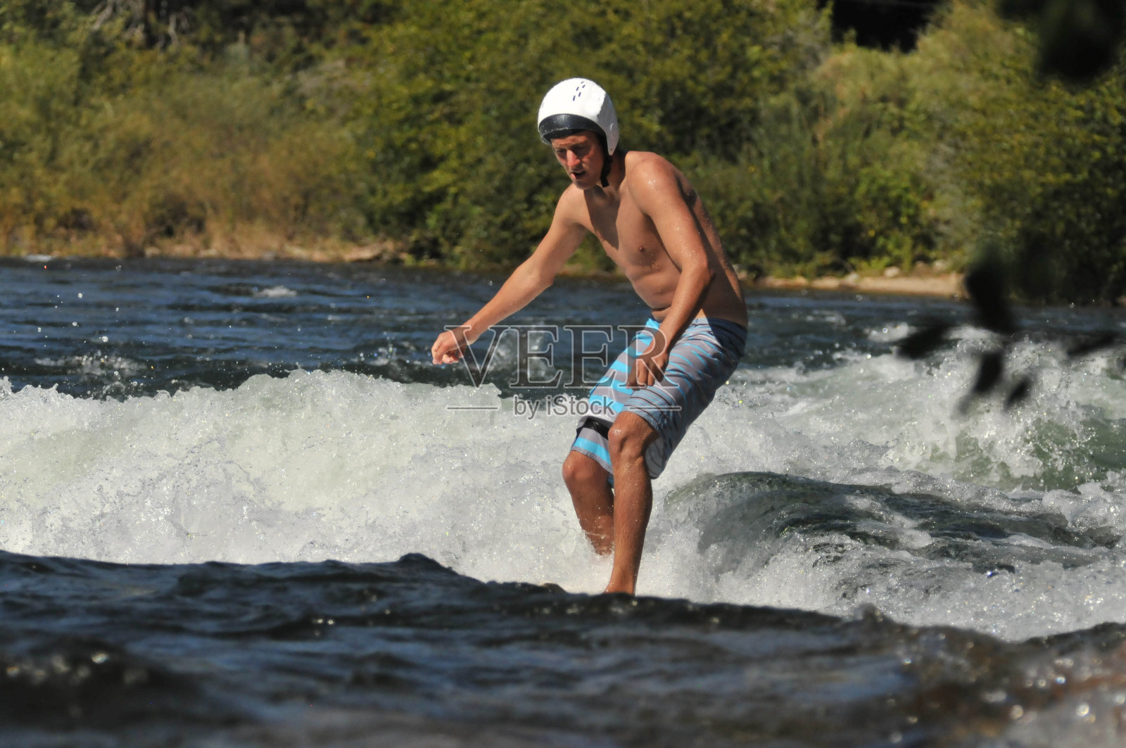 一个戴着头盔在河中冲浪的年轻人照片摄影图片