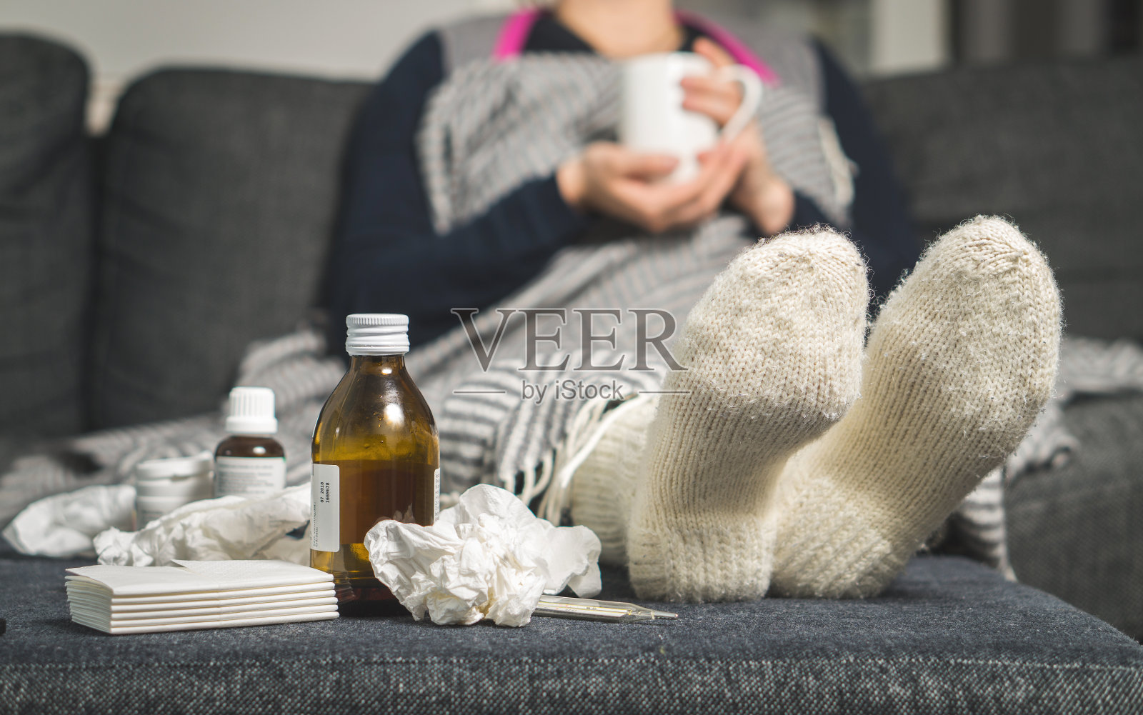 感冒药和生病的女人喝热饮来恢复流感，发烧和病毒。桌子上有脏的纸巾和纸巾。生病的人在冬天穿着暖和的羊毛长袜。照片摄影图片