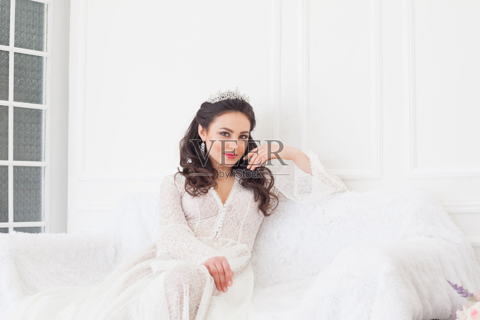 身着婚纱、头戴皇冠的新娘坐在白色沙发上照片摄影图片