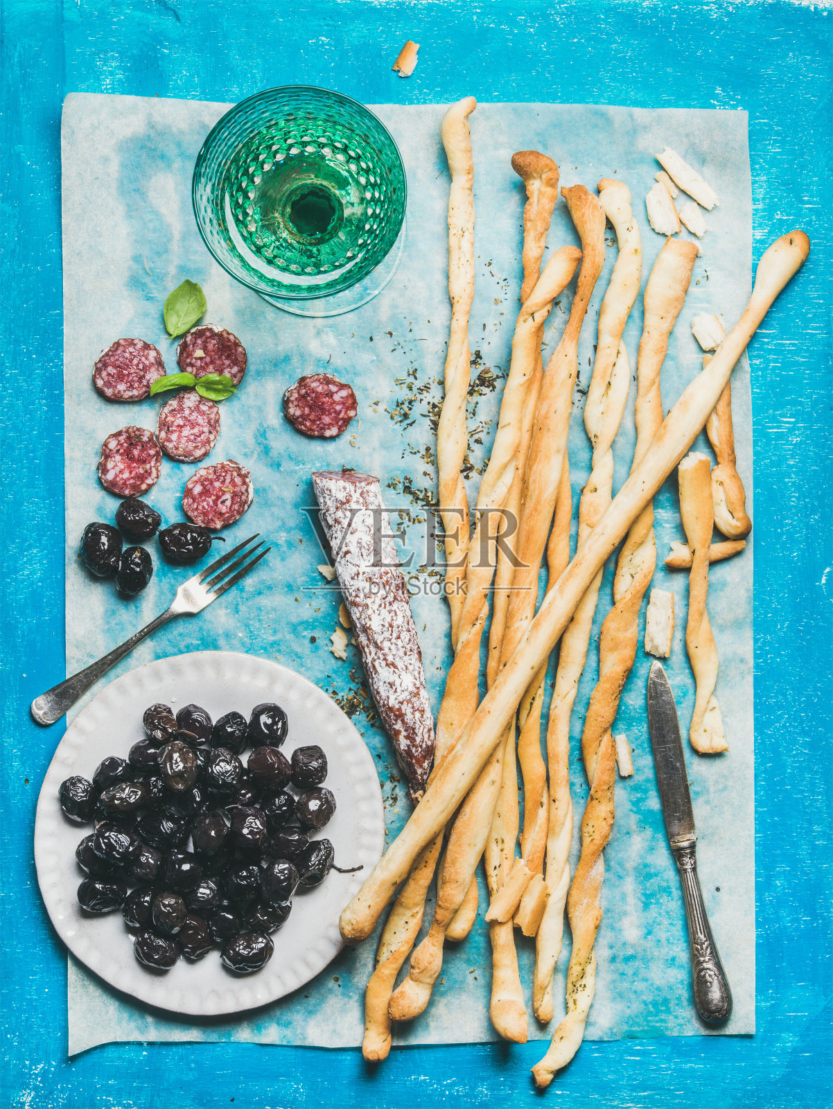 格里西尼面包棒，香肠，橄榄和白葡萄酒，蓝色背景照片摄影图片