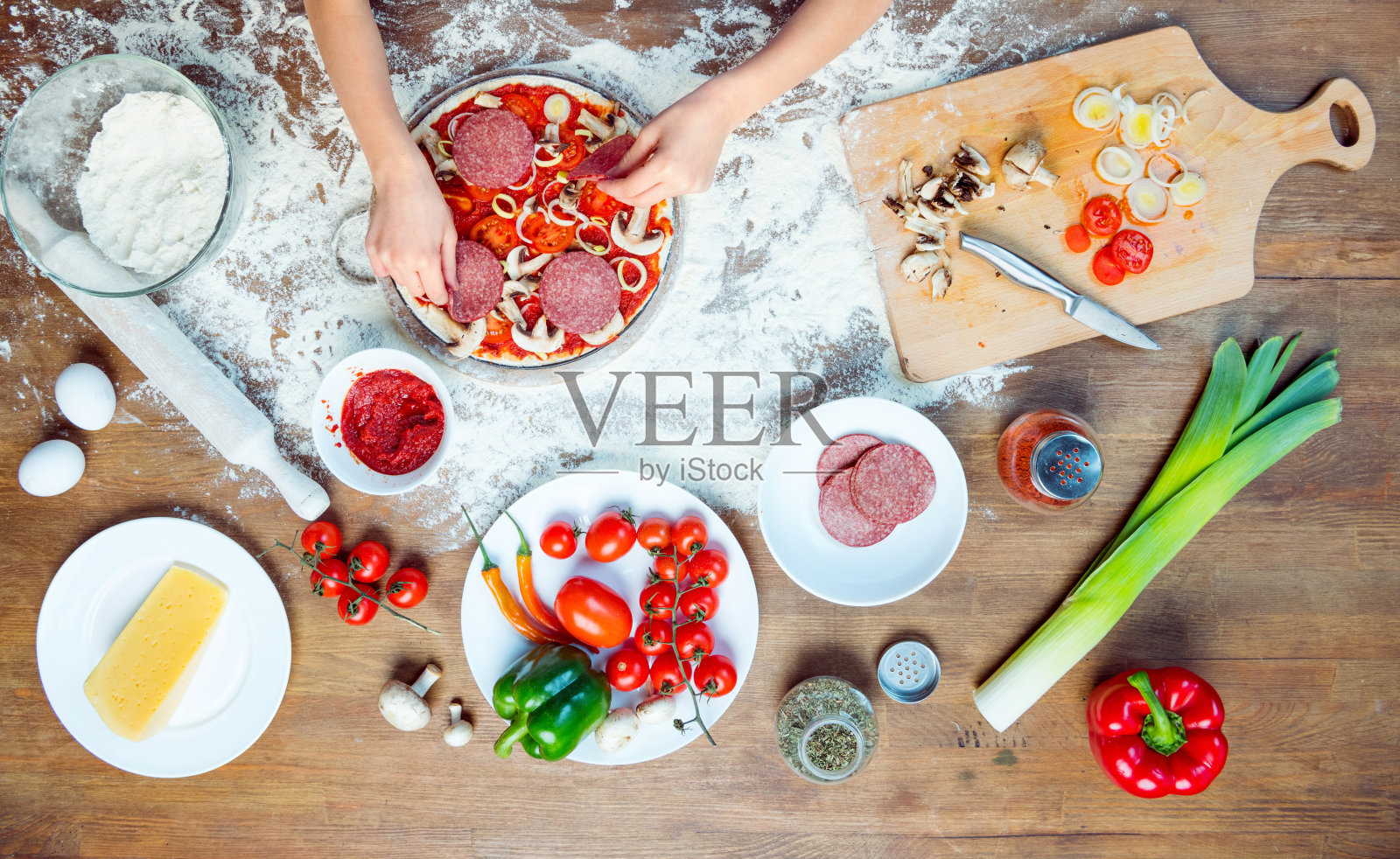 俯视图的孩子做比萨饼的配料，西红柿，意大利腊肠和蘑菇在木制的桌面上照片摄影图片