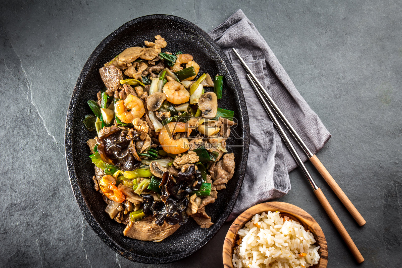 中国菜。Te pam圣。一锅炸牛肉，猪肉，鸡肉，虾，香菇，冠军和葱。配以灰色石板背景的米饭。照片摄影图片