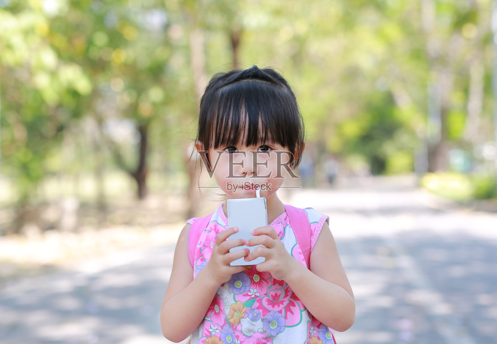 小女孩在公园里用稻草喝牛奶的特写。肖像户外。照片摄影图片