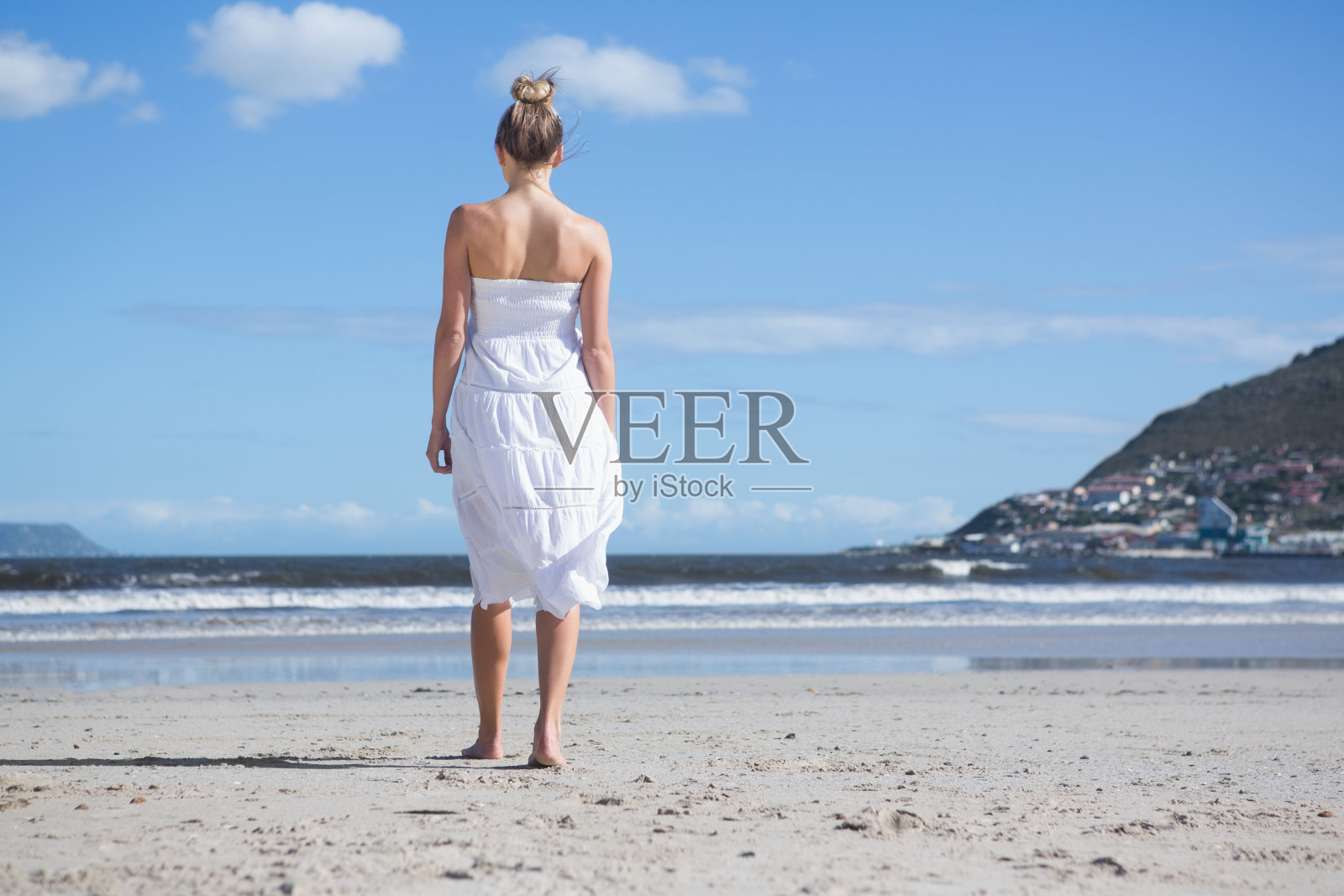 穿着白色裙子的金发女郎在海滩上散步照片摄影图片
