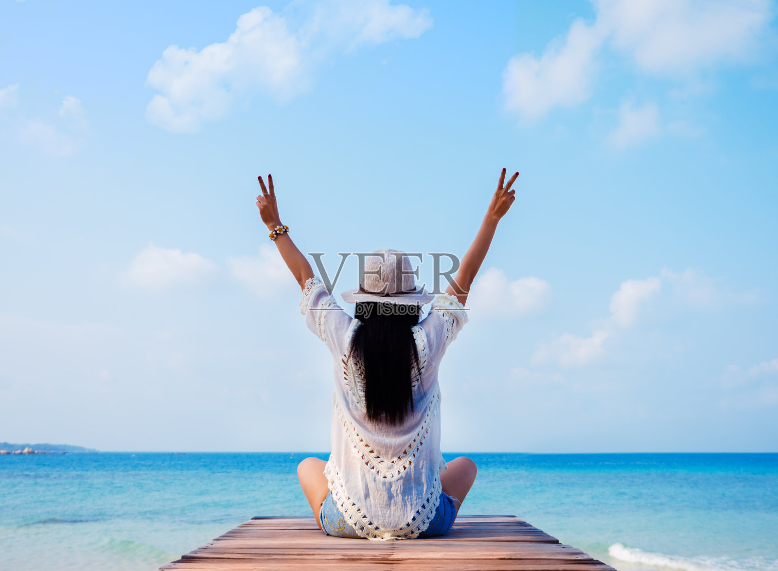 戴太阳帽的女人举起双手，坐在那里望着大海。副本的空间。照片摄影图片