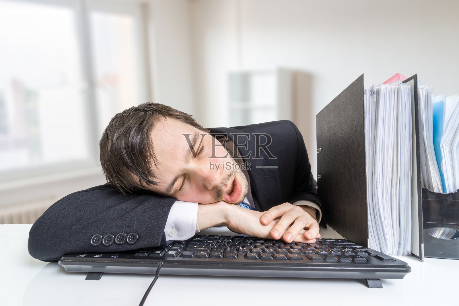 劳累过度的男人在办公室的键盘上睡觉。照片摄影图片