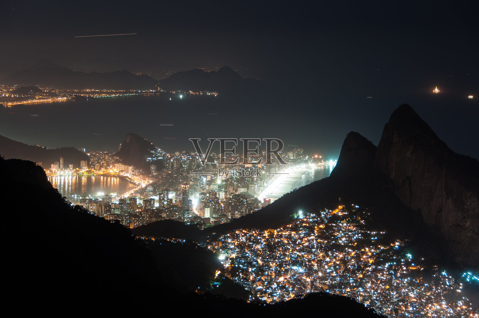 夜间的Rocinha贫民窟和山后的伊帕内玛区照片摄影图片