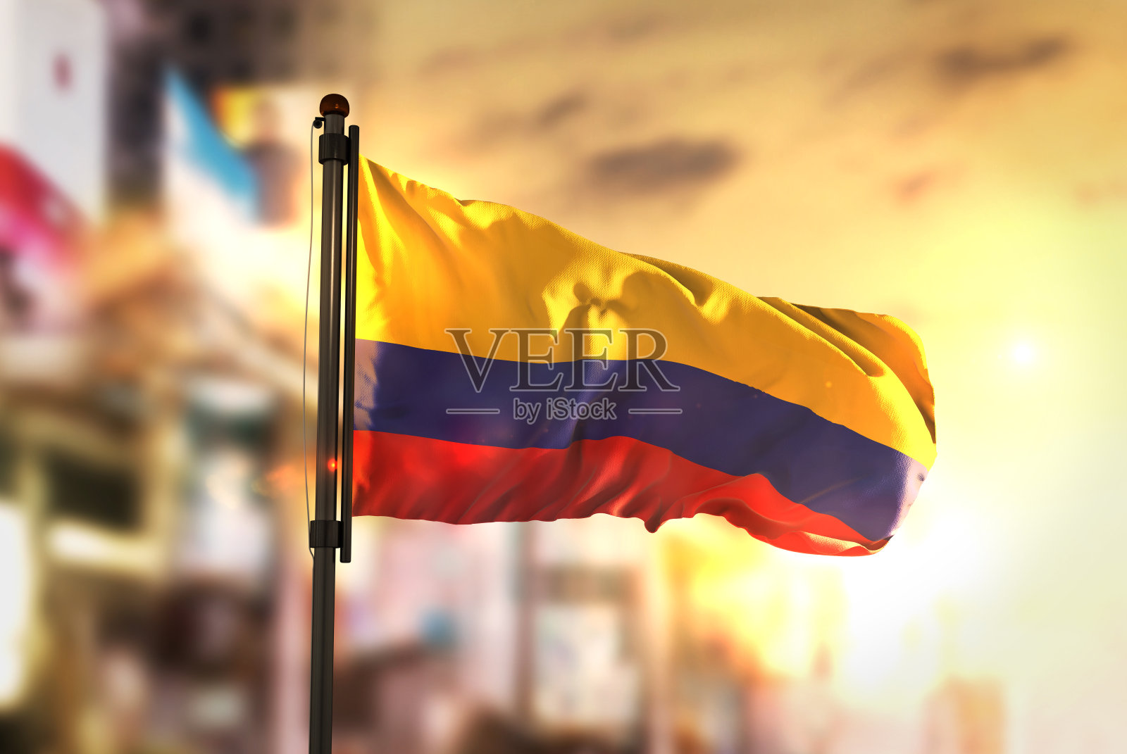 在日出的背光下，城市模糊的背景下的哥伦比亚国旗照片摄影图片