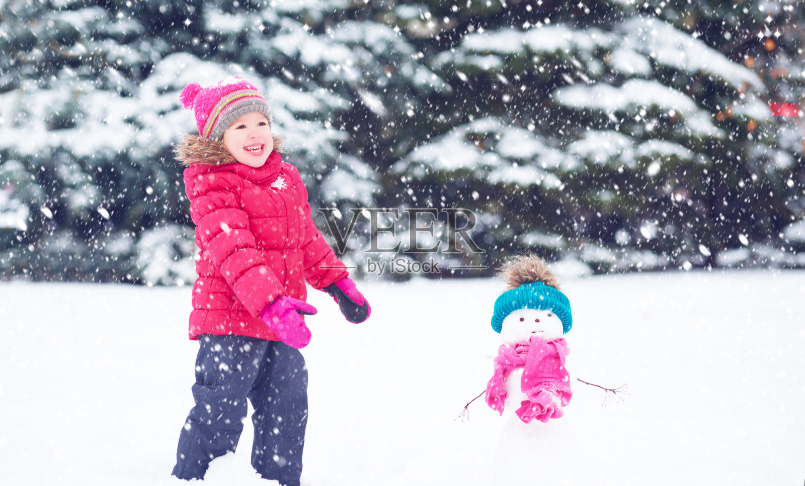 快乐的小女孩和一个雪人在冬天散步照片摄影图片