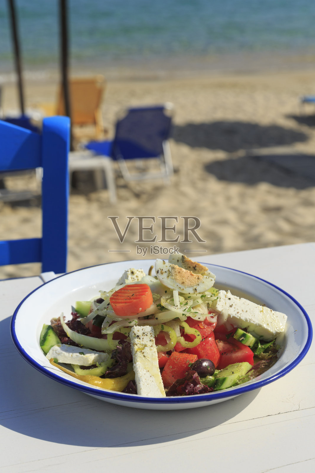 大海边的希腊沙拉，白色木桌背景上的传统希腊沙拉，散焦椅子和海滩为背景照片摄影图片