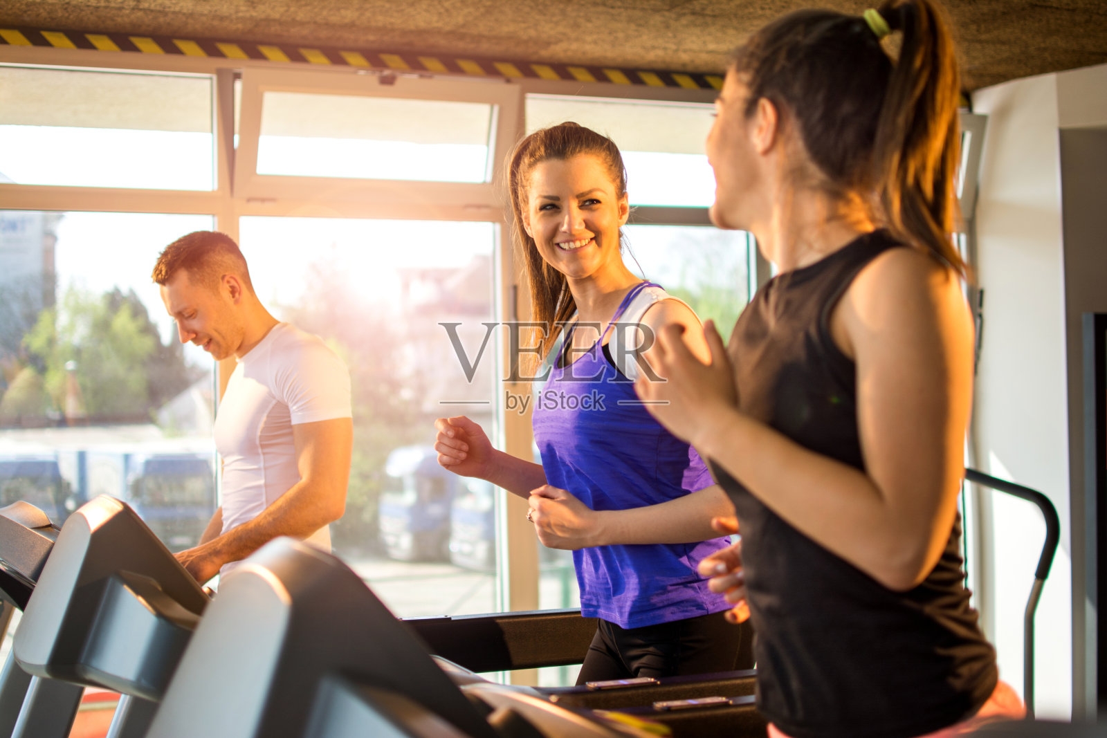 快乐的闺蜜一起在健身房的跑步机上跑步。照片摄影图片