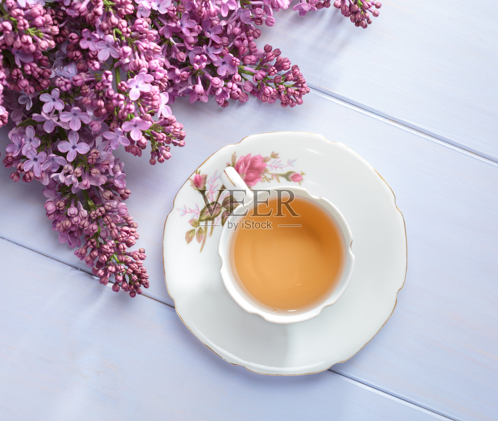 木桌上放着一杯茶和盛开的丁香枝。照片摄影图片