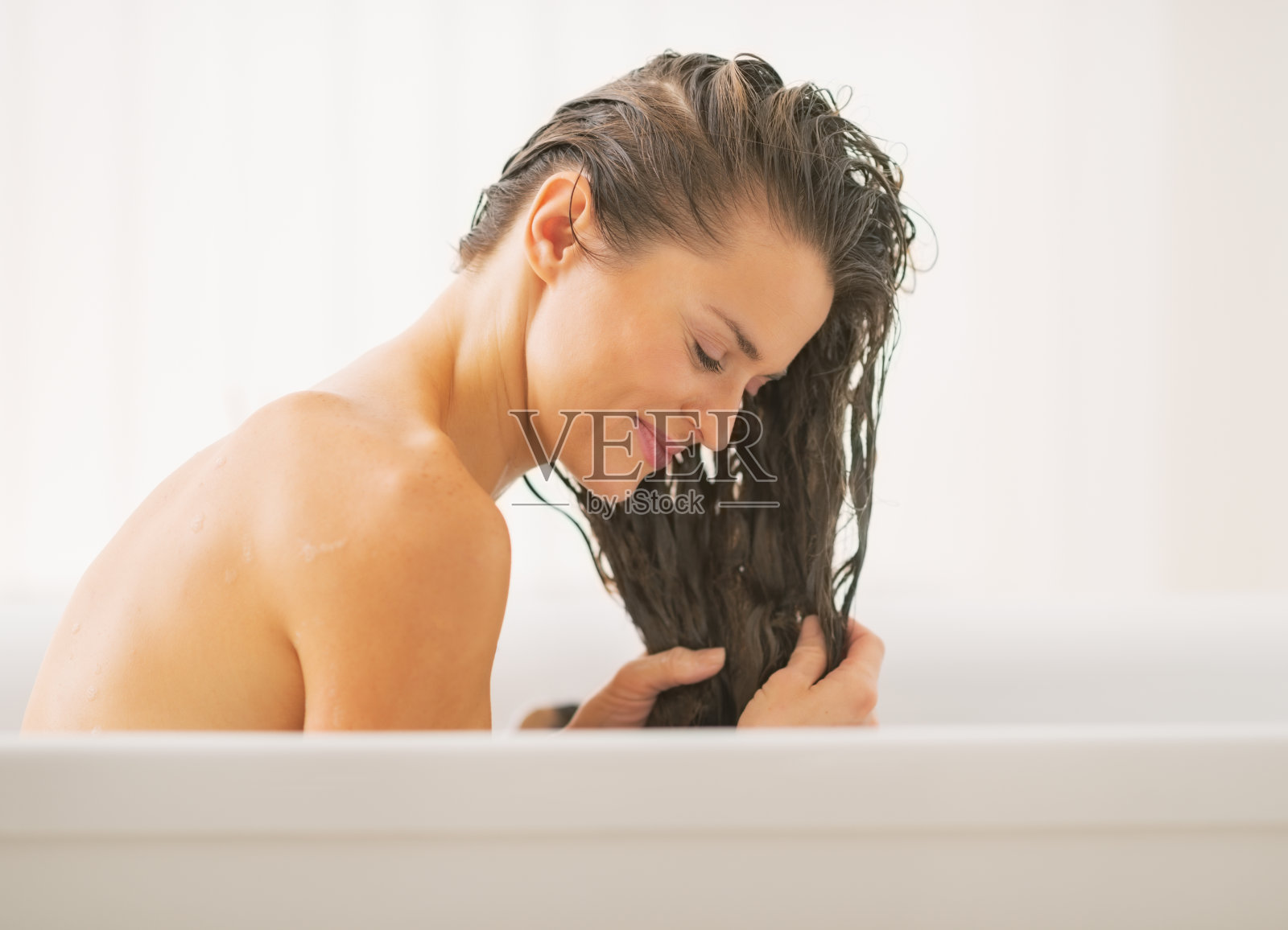 快乐的年轻女子在浴缸里洗头照片摄影图片
