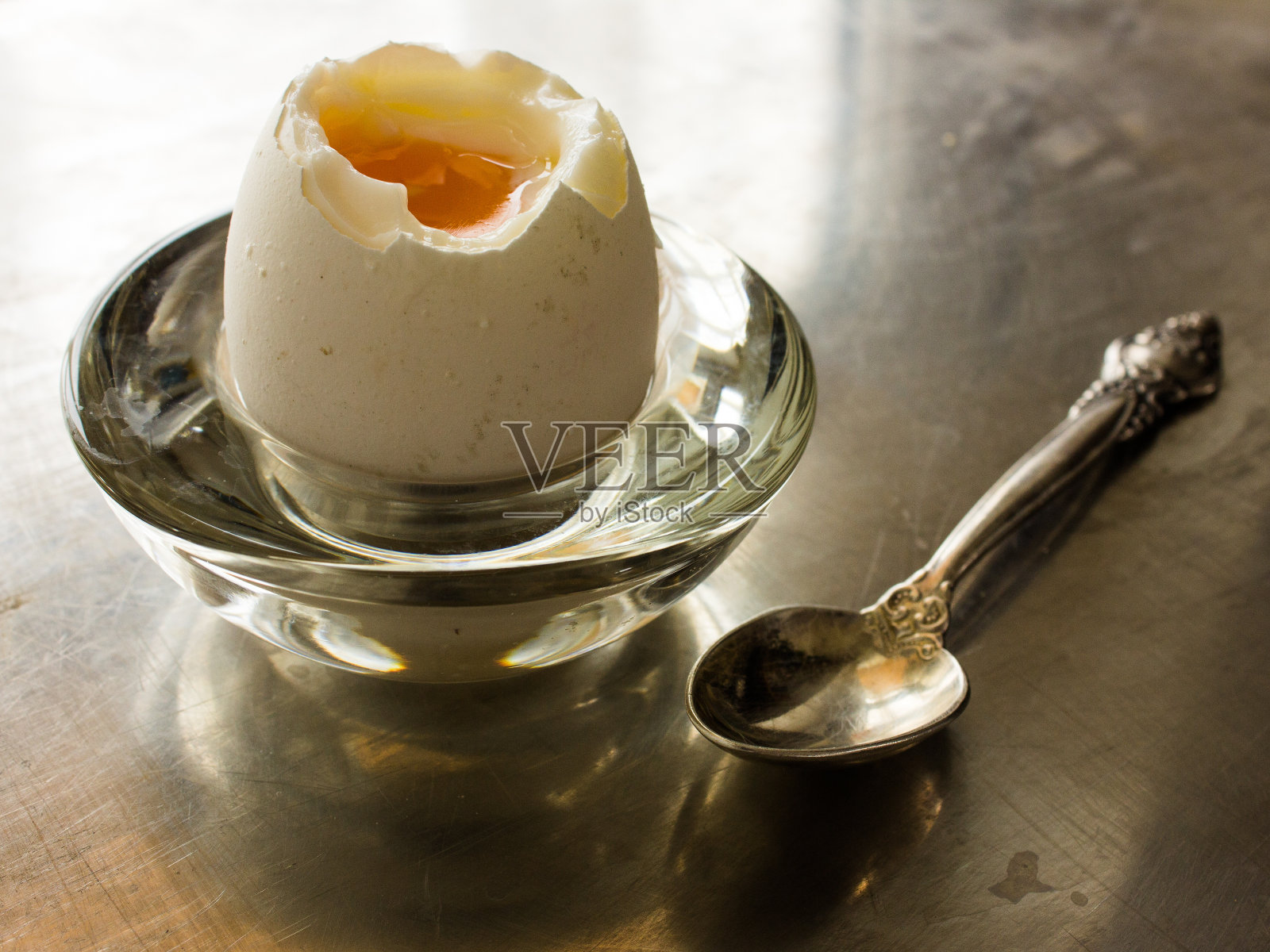 用银勺子和鸡蛋壳装在玻璃盘子里煮半熟的鸡蛋。金属背景照片摄影图片