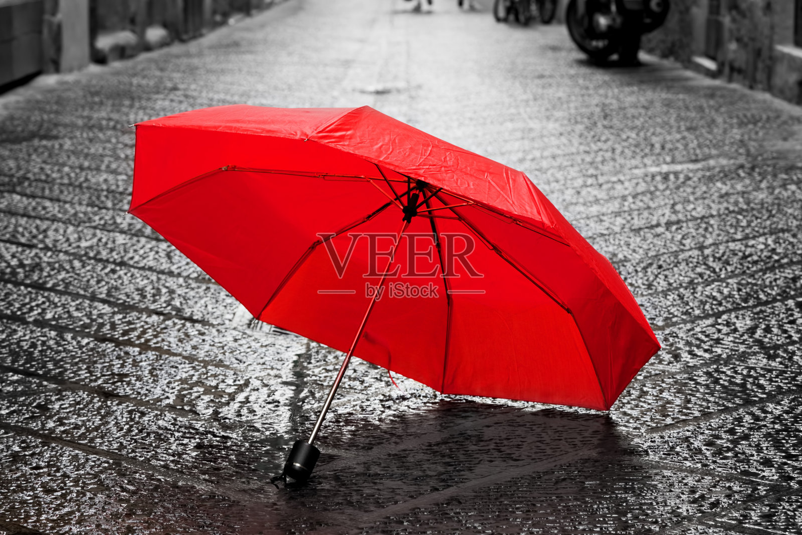 红伞在老城的鹅卵石街道上。风和雨照片摄影图片
