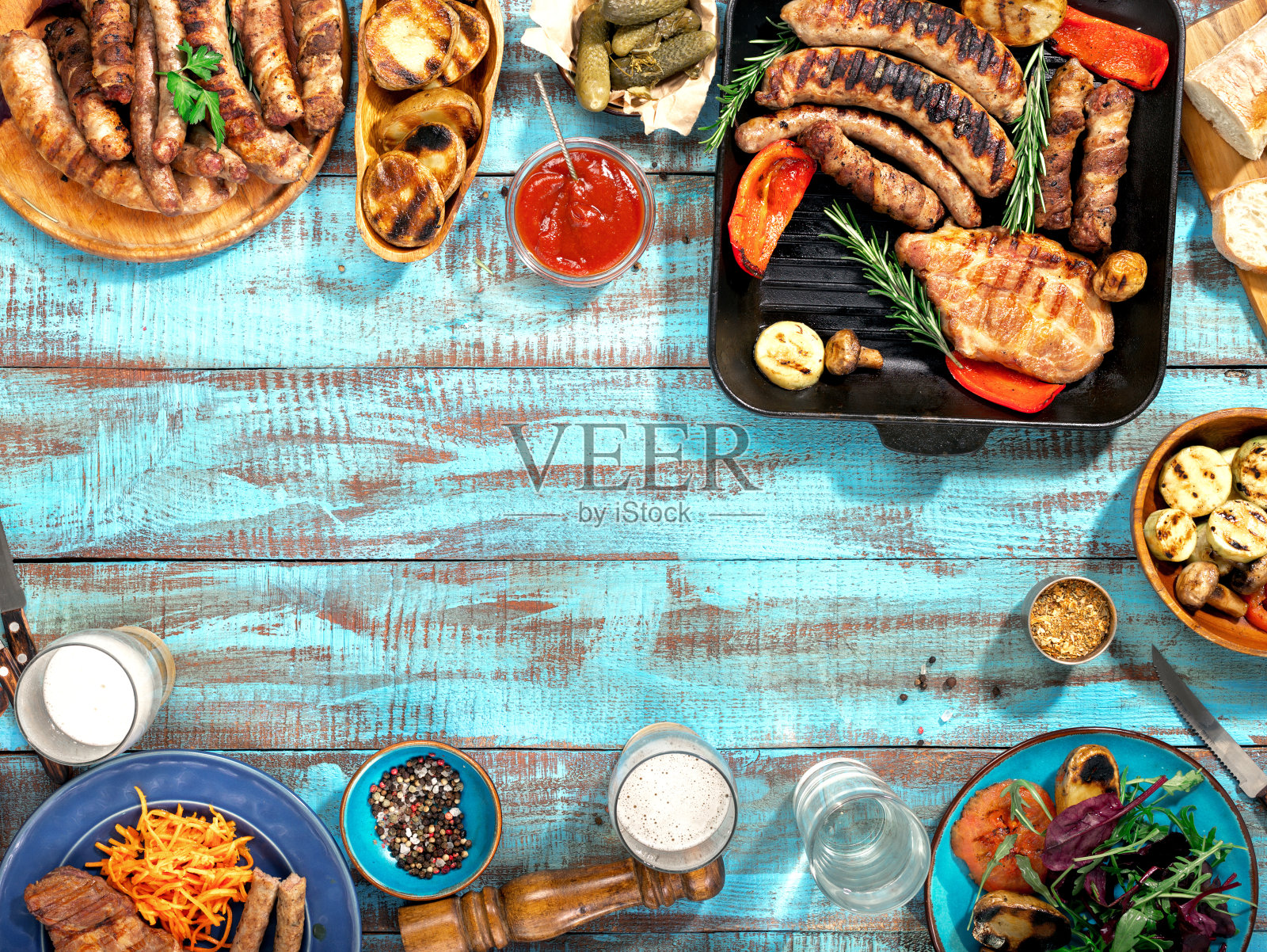 在阳光明媚的日子里，蓝色木桌上的烤架上烤着不同的食物，烤牛排，烤香肠，烤蔬菜和啤酒照片摄影图片
